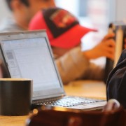 Mann sitzt vor einem Laptop in einem Cafe und arbeitet.