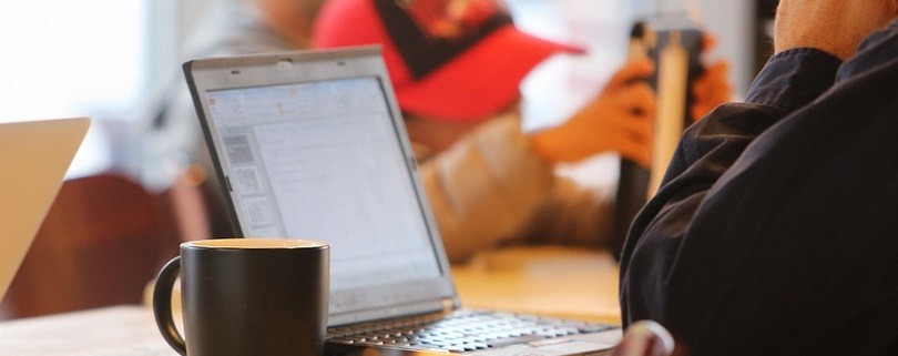 Mann sitzt vor einem Laptop in einem Cafe und arbeitet.